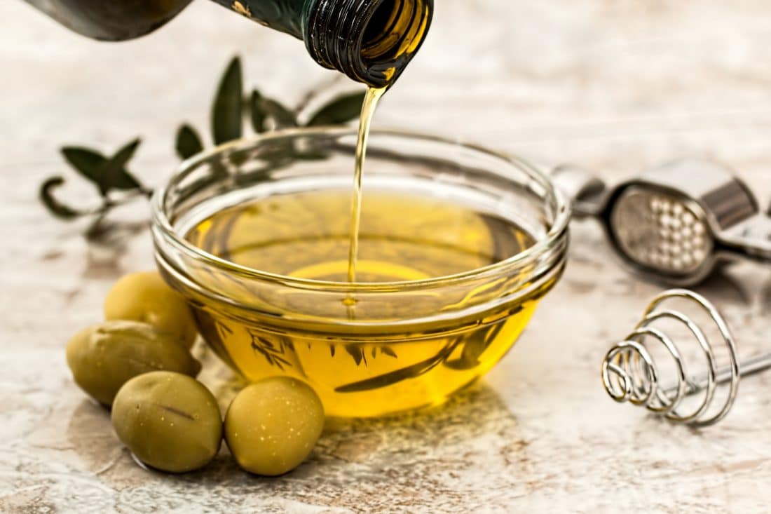 Eine Flasche Olivenöl wird in eine Schüssel mit Oliven gegossen.